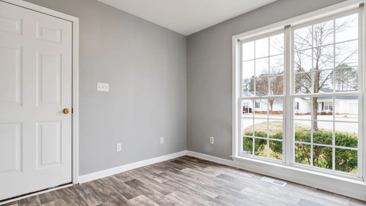 Gray vinyl plank in an empty room with a large window and a white door