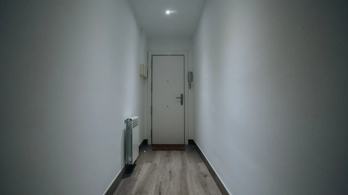 Gray plank flooring in a narrow hallway ending at a white door