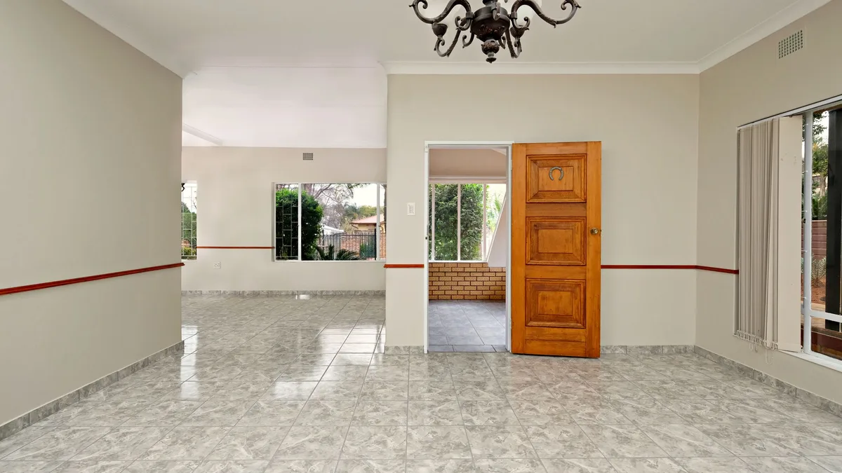 Glossy gray floor tile in an open room with a chandelier and a wood door