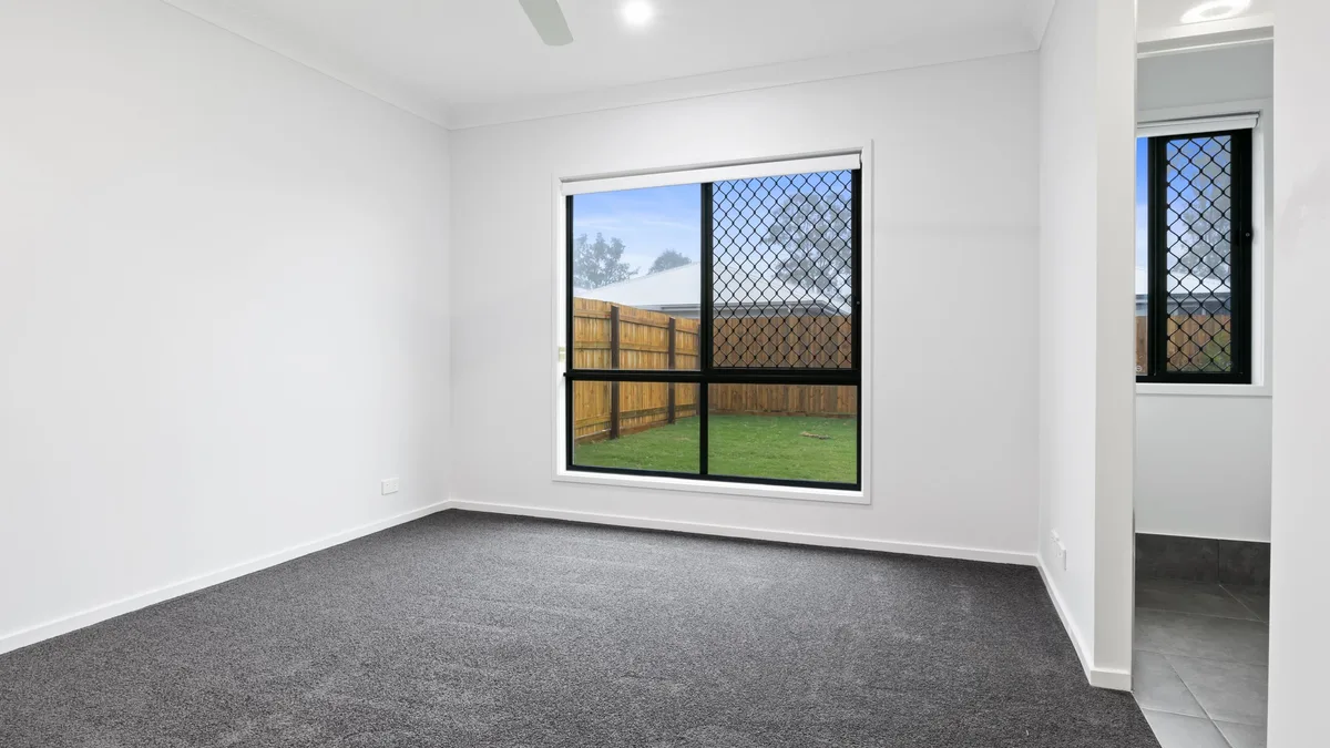 Dark gray carpet in an empty bedroom with a window onto a fenced yard